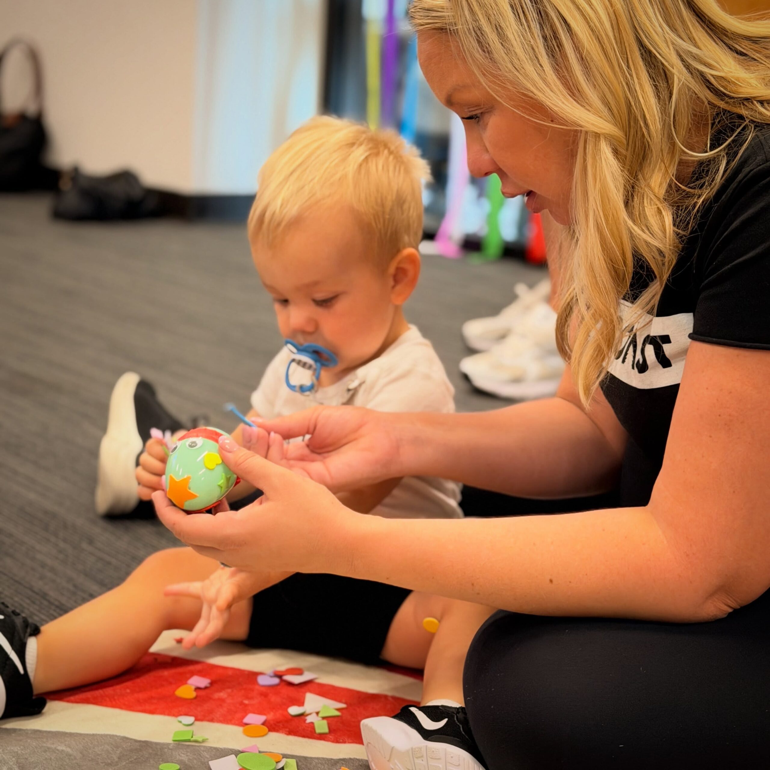 An adult helps a young child explore a colorful craft.