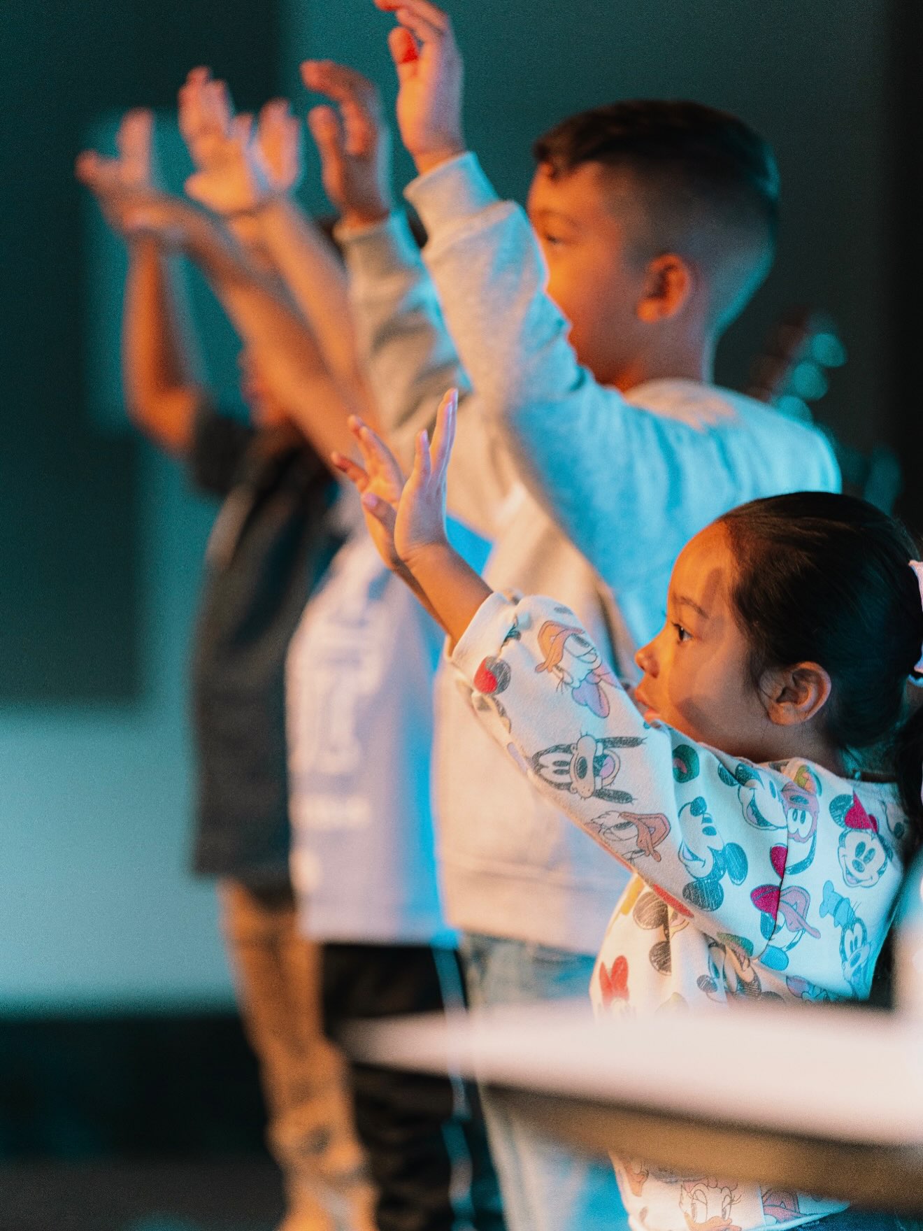 Children raise their hands together during worship in kids ministry.