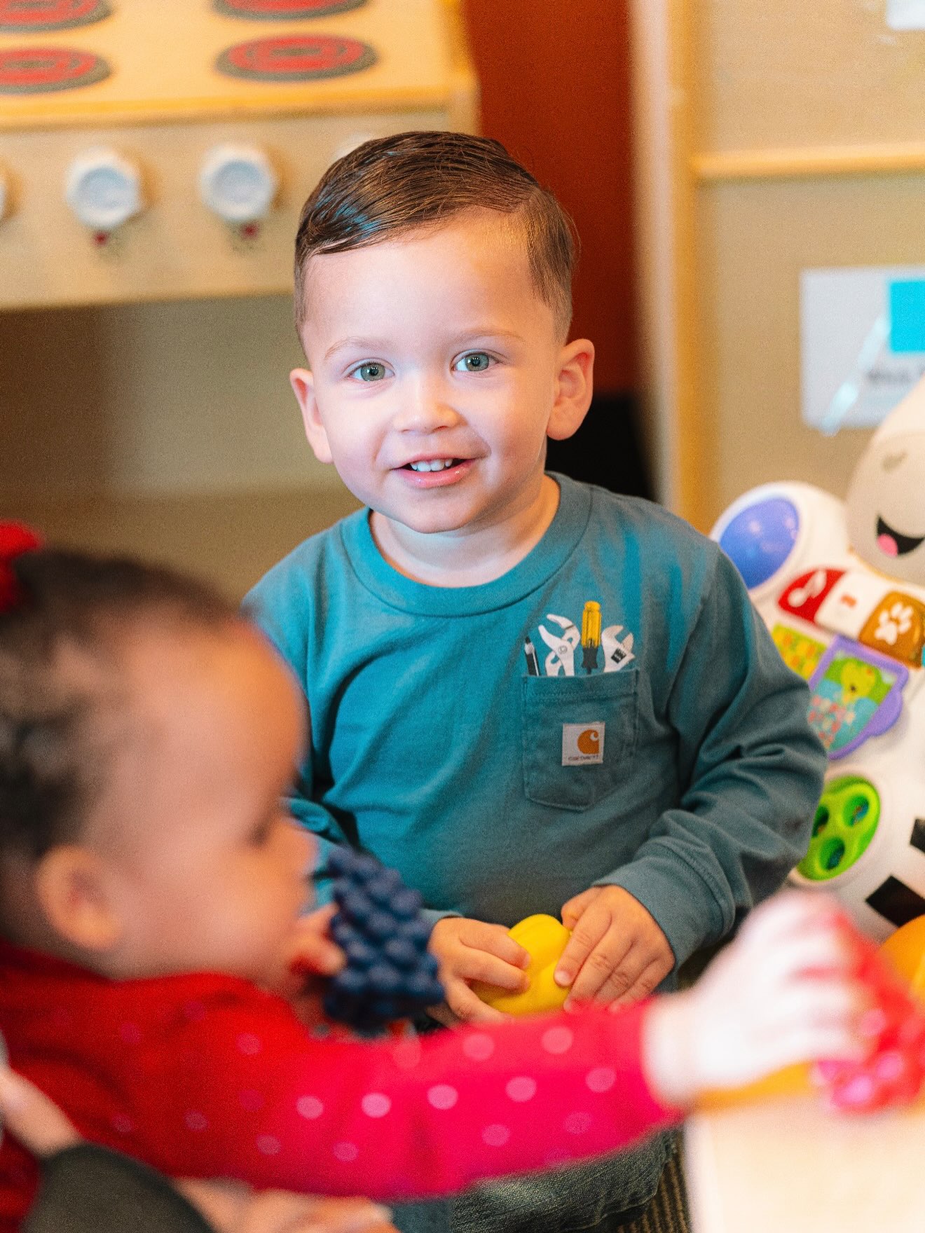 A smiling child plays with toys alongside other children.