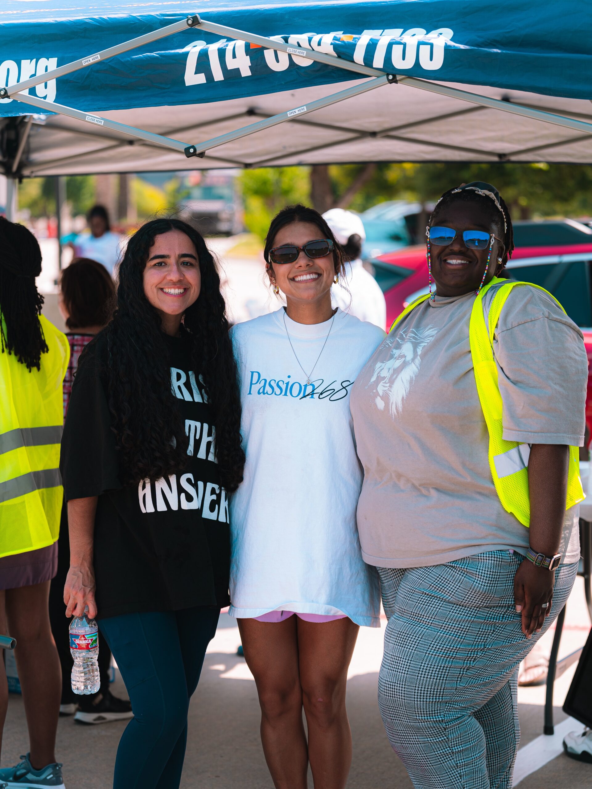 Three volunteers smile together under an outreach tent.