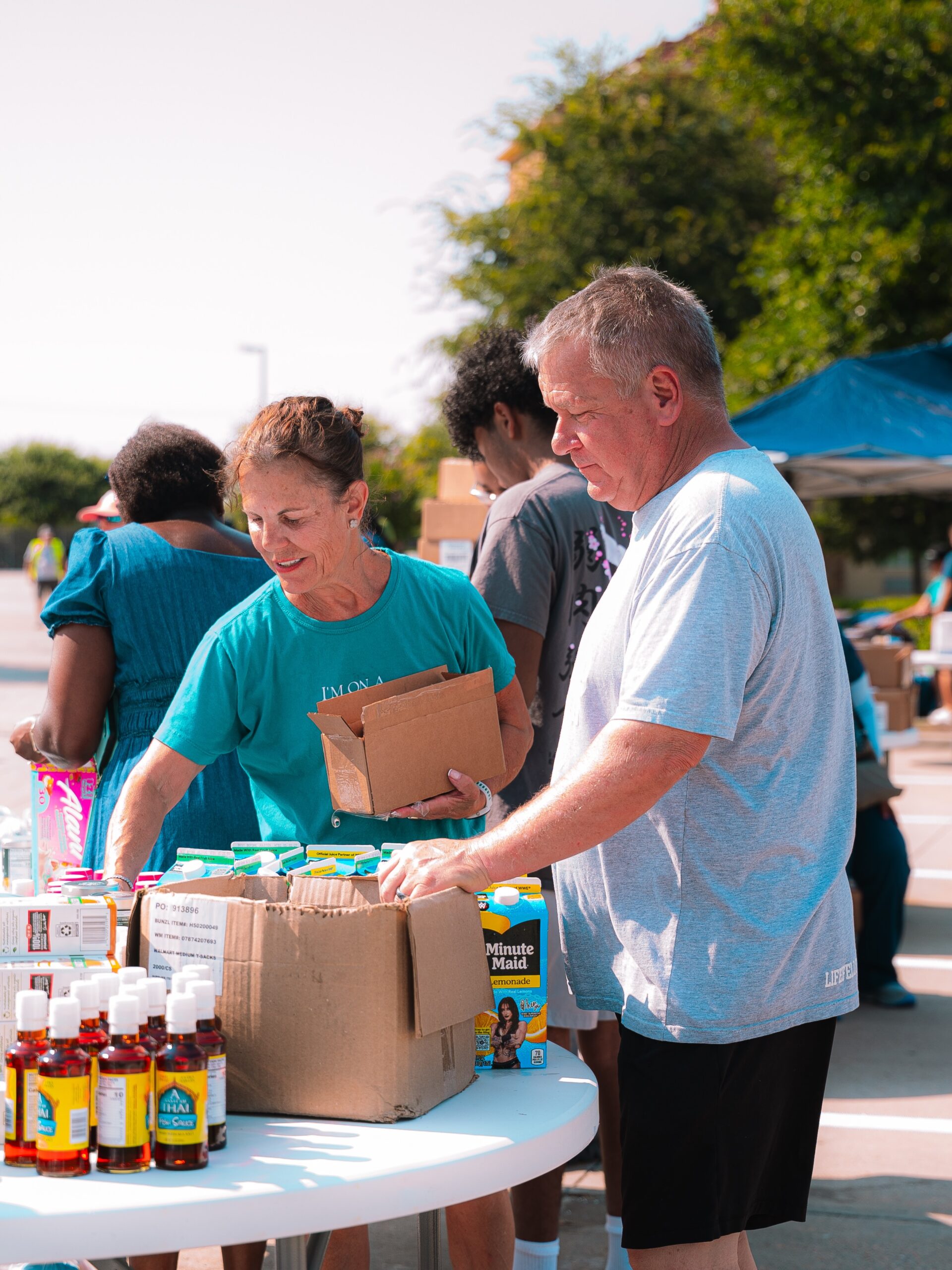 Two volunteers prepare boxes of food together at an outdoor table.
