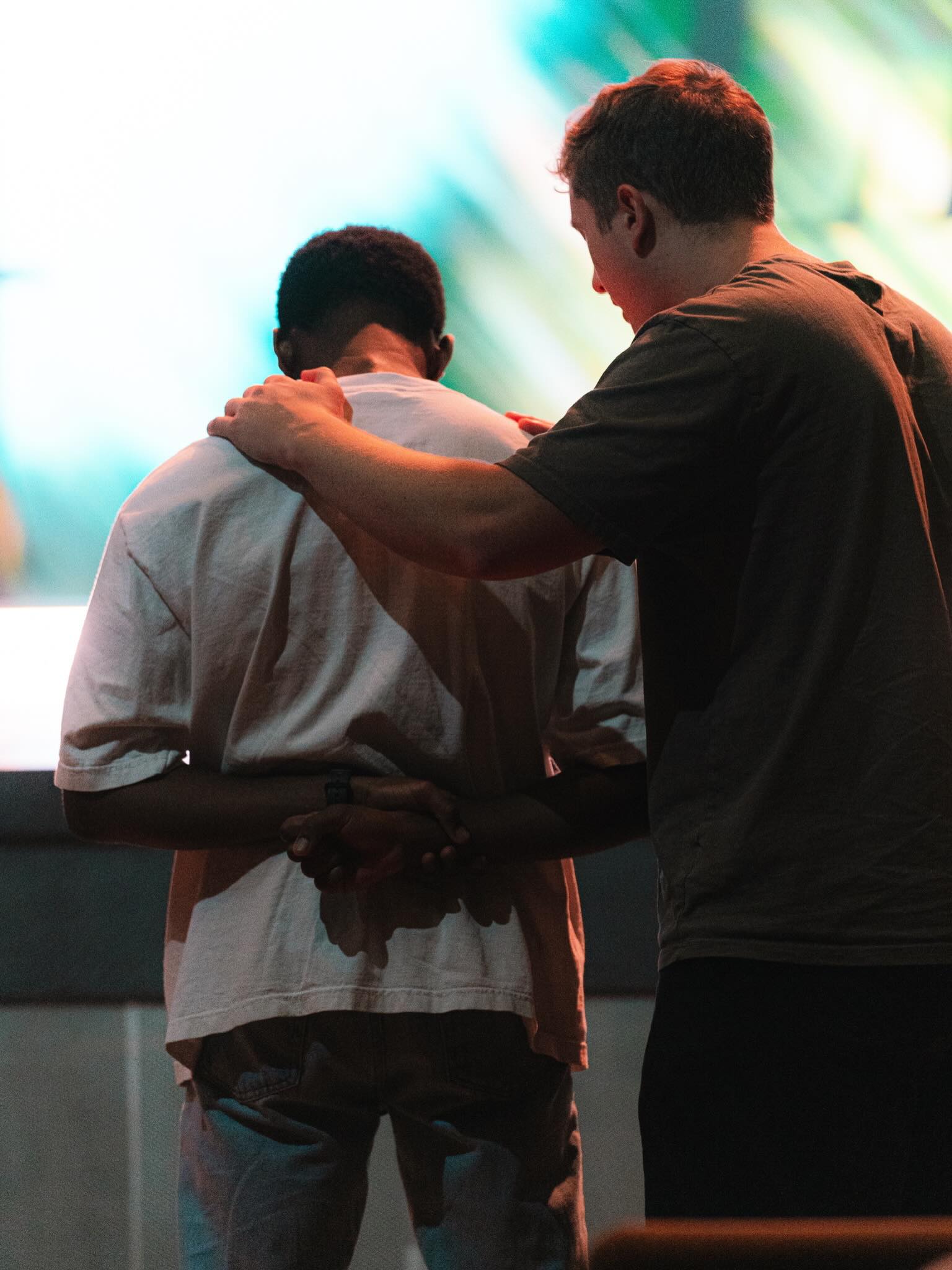One person rests a hand on another person's shoulder during prayer.