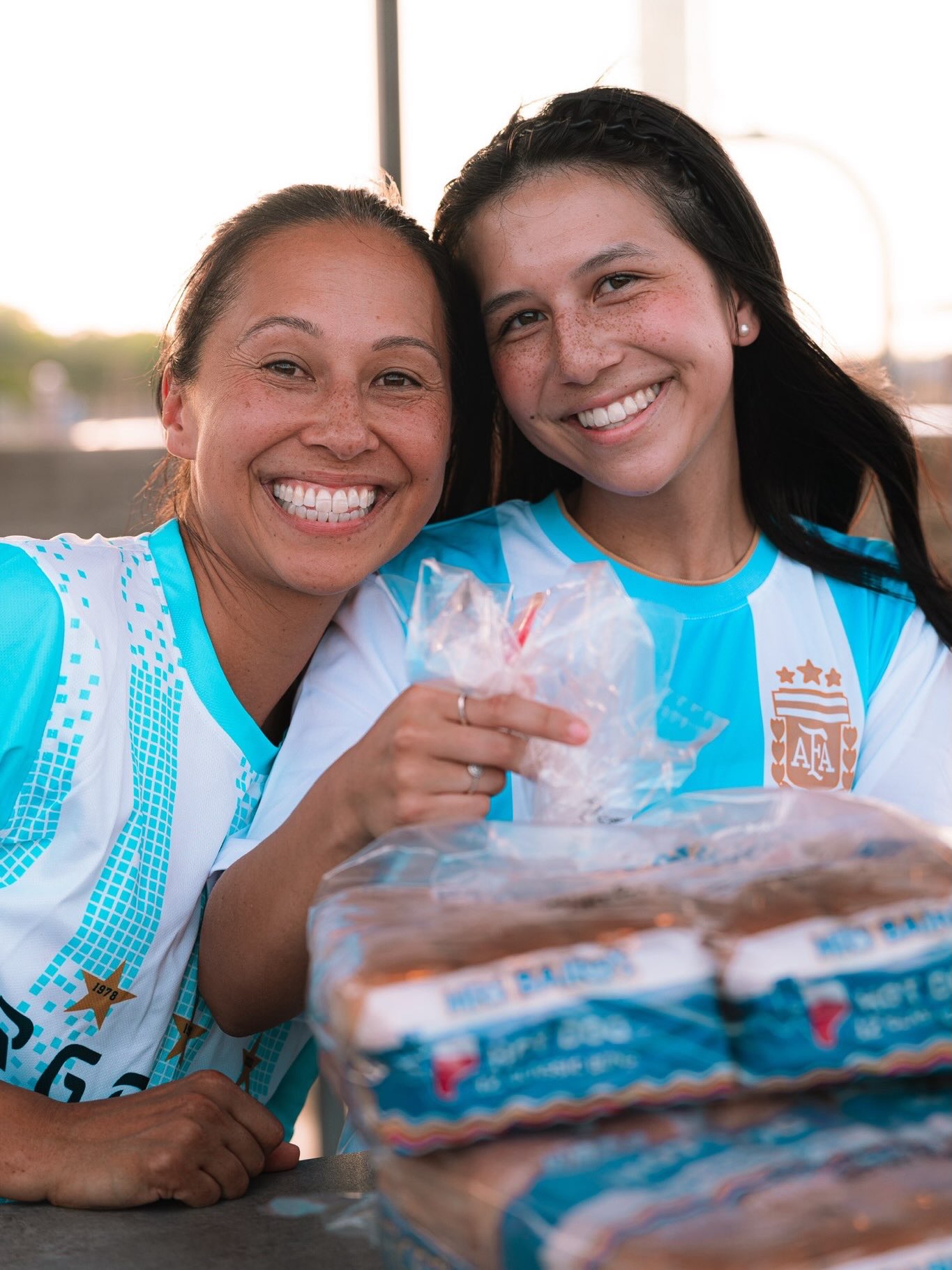 Two young adults smile together behind a table of food at a community night.