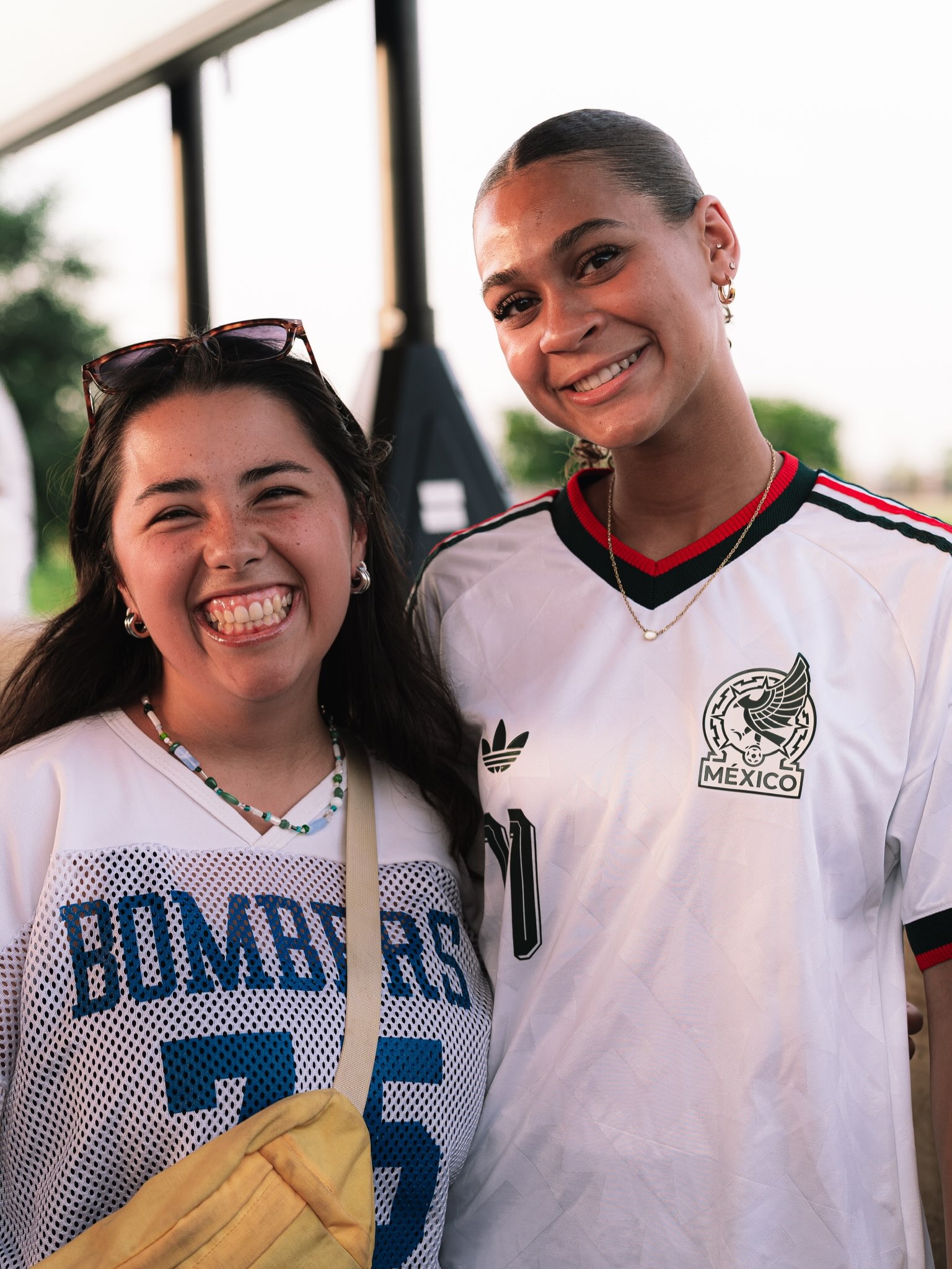 Two young adults smile together at an outdoor community gathering.